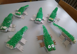 Na stoliku rozłożone zielone krokodyle wykonane z rolki po papierze oraz folii bąbelkowej.